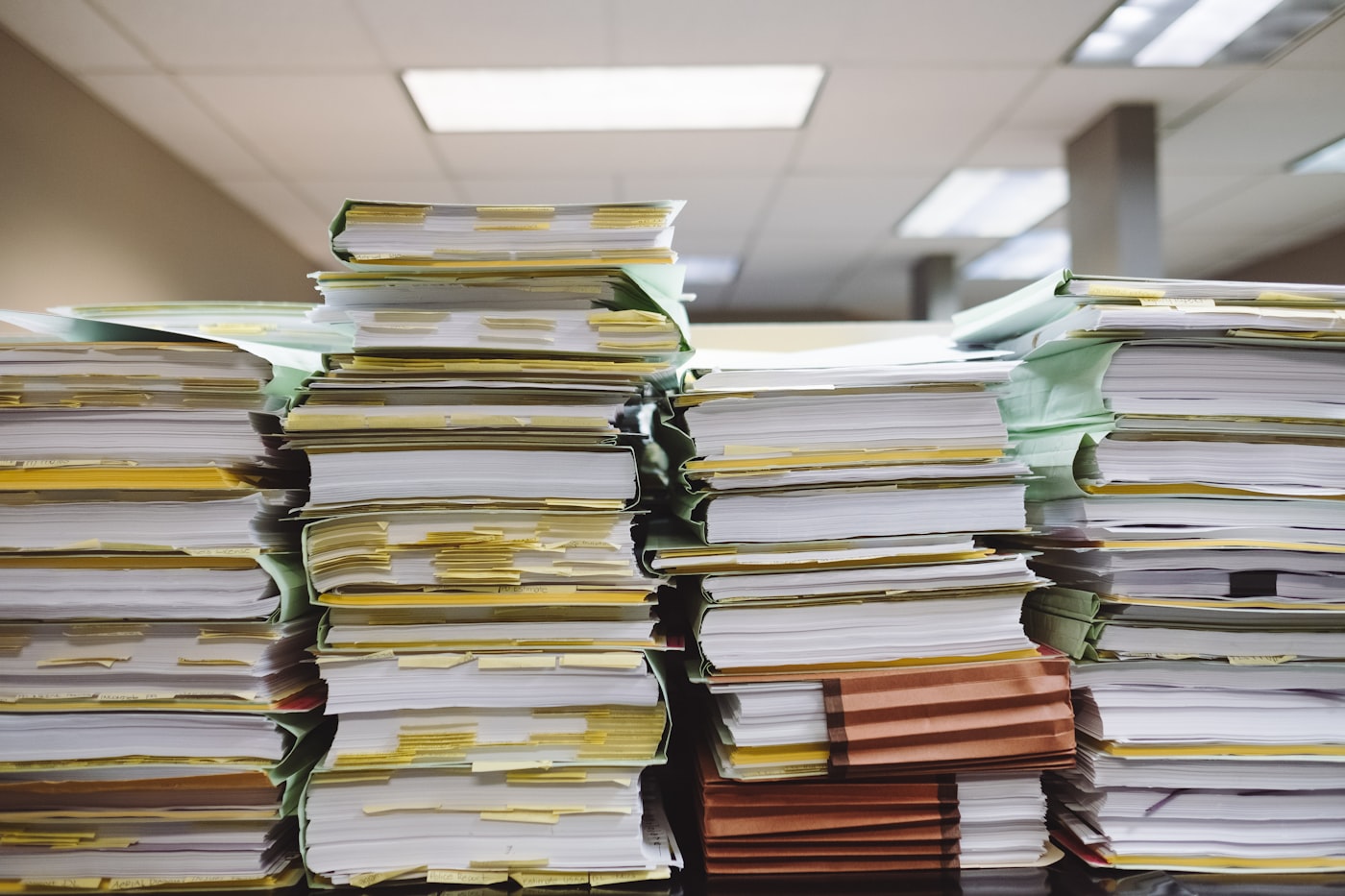 Stacks of paper documents and file folders, a metaphor for a contracts folder nobody can query