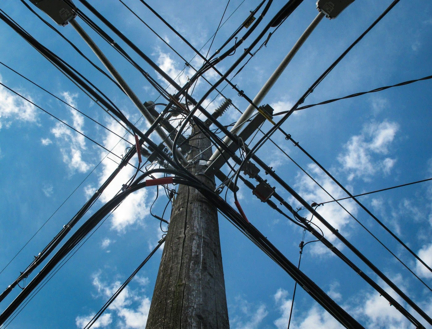 A utility pole with wires converging from many directions against a blue sky, a metaphor for many independent websites sharing one company's nameservers as an unchosen single point of failure