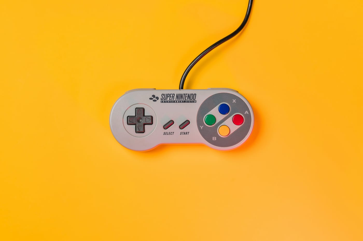 A Super Nintendo controller on a yellow background — the console generation this whole 90s-arcade comparison belongs to, one deliberate control surface instead of an interpreter's worth of hidden machinery