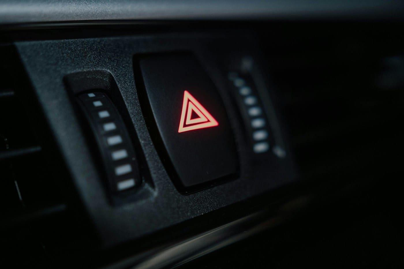 A car's hazard warning light glowing red in an otherwise dark dashboard