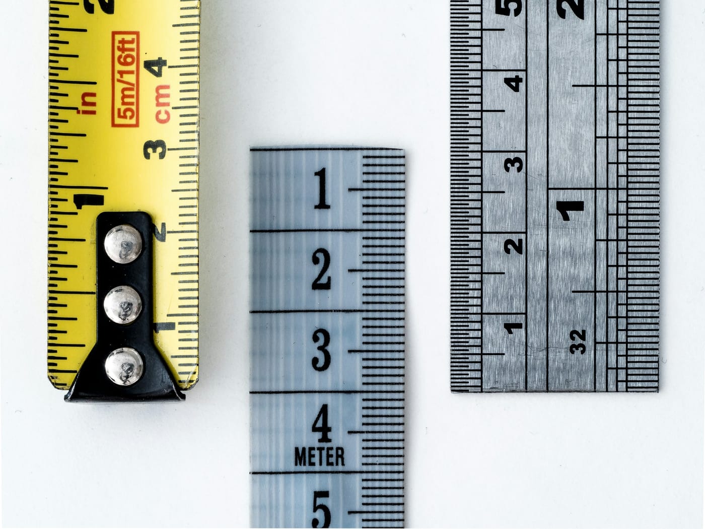 A yellow tape measure, a cloth measuring tape and a steel ruler side by side, each marked in different units, a metaphor for similarity scores that change scale between embedding models