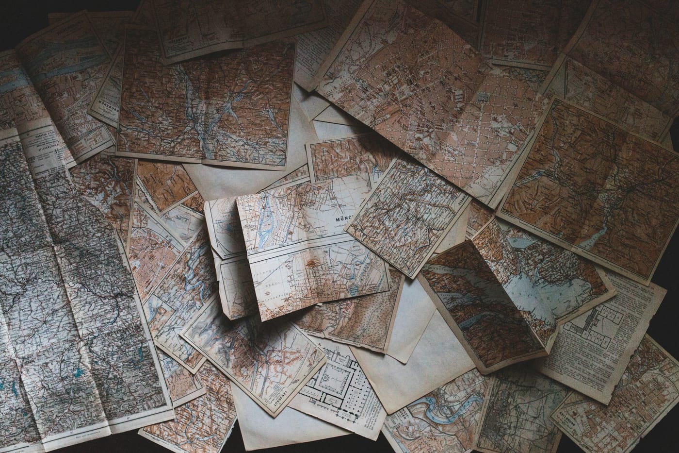 Dozens of old printed maps of different regions piled on top of each other, a metaphor for embedding models that each draw their own map of meaning