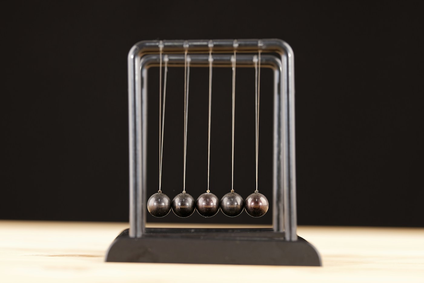 A Newton's cradle with five steel balls at rest, a metaphor for a hiring process where both sides carry weight and effort passes in both directions