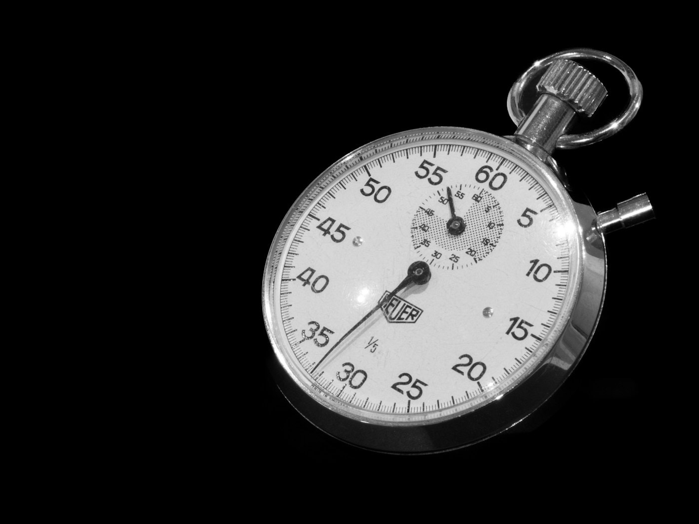 A black-and-white stopwatch on a black background, a metaphor for the live coding round measuring thinking against a clock