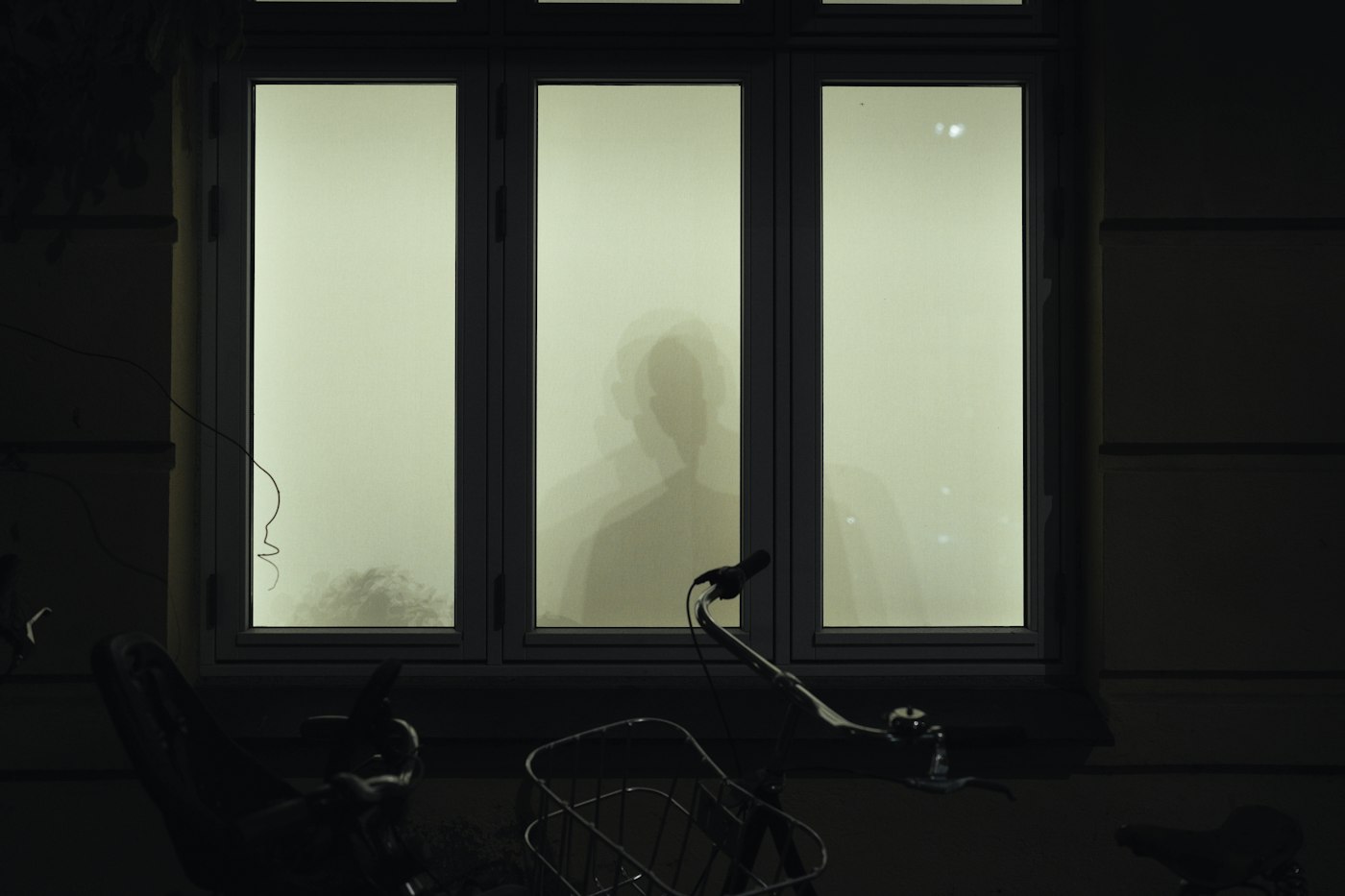 A silhouette of a person seen through a frosted window at night, a metaphor for reasoning that happens inside a thinking model where we cannot inspect it